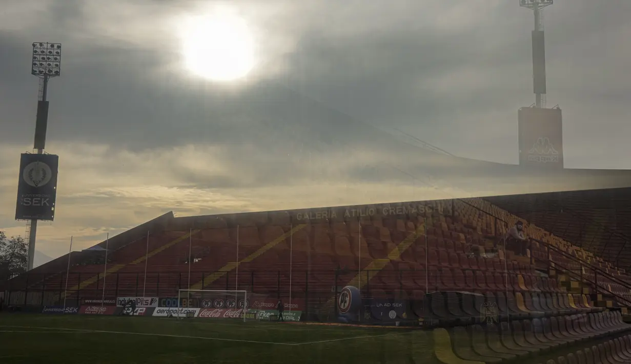Seorang penggemar klub Union Espanola tercermin dalam perisai kaca sebelum dimulainya pertandingan di stadion Santa Laura, Chile, Sabtu (14/8/2021). Setelah lebih dari satu tahun lockdown, penggemar diizinkan kembali ke stadion di tengah protokol kesehatan dan jarak sosial ketat. (AP/Esteban Felix)