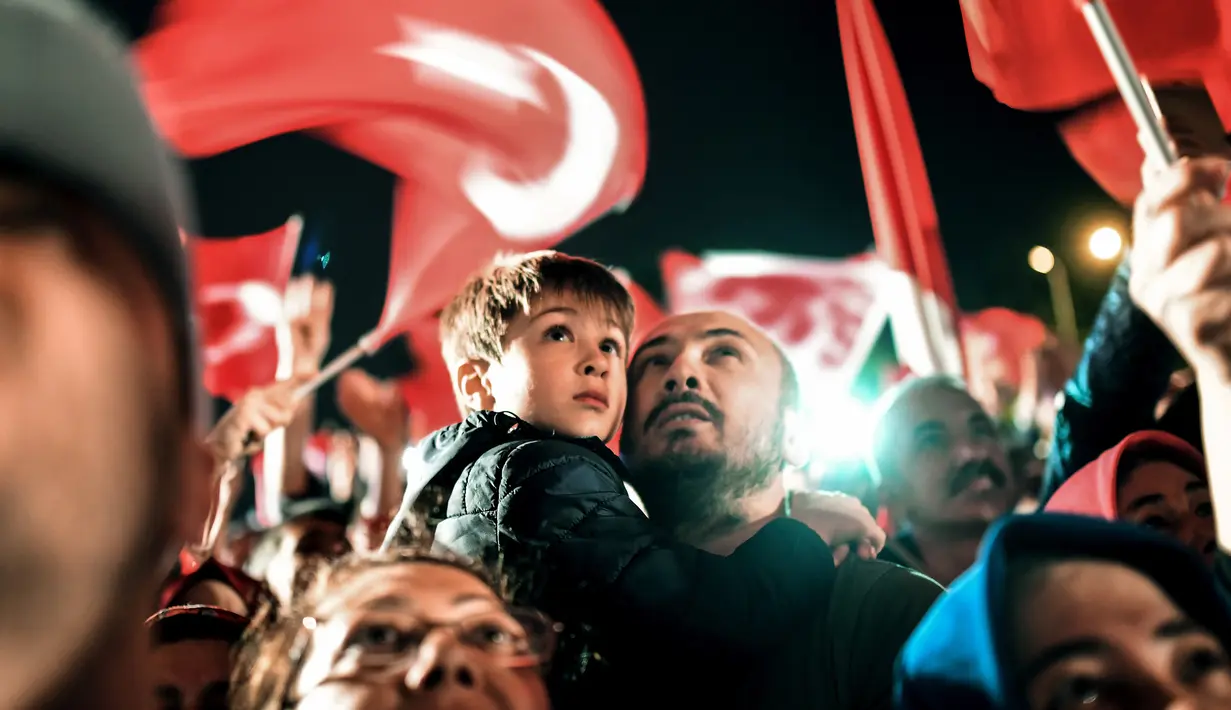 Seorang pria dan anaknya merayakan dan menyambut Presiden Turki Turki Recep Tayyip Erdogan berpidato di dekat markas besar konservatif Partai Keadilan dan Pembangunan (AKP) di Istanbul, Turki (16/4). (AFP Photo / Bulent Kilic)