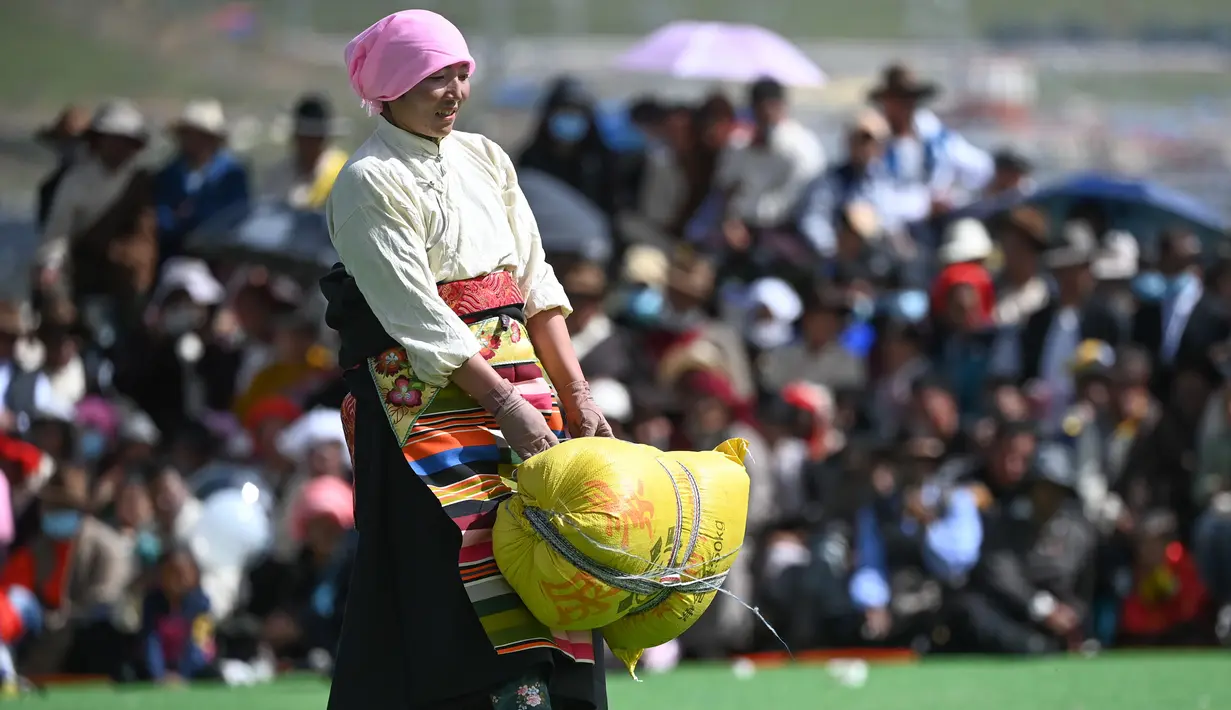Seorang partisipan mengangkat karung berisi barli dataran tinggi dalam sebuah kompetisi yang digelar saat festival balap kuda Dangjiren di Wilayah Damxung, Daerah Otonom Tibet, China barat daya, pada 11 Agustus 2020. (Xinhua/Purbu Zhaxi)