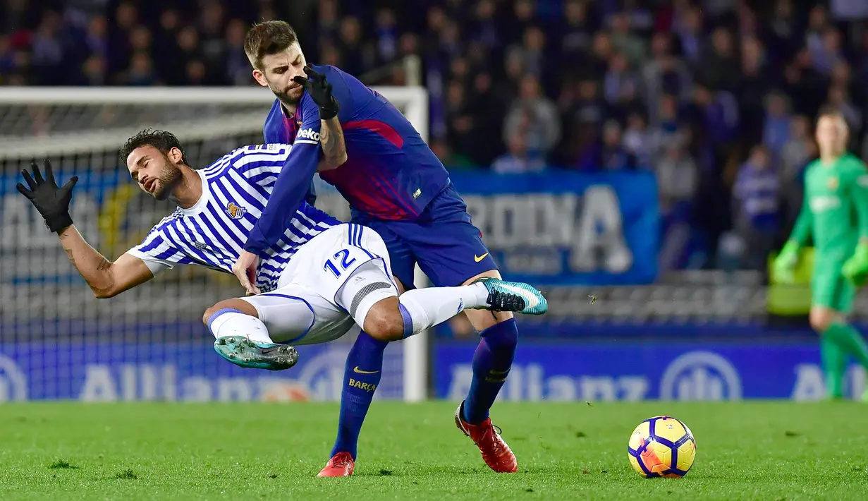 Pemain Barcelona, Gerard Pique berebut bola dengan pemain Real Sociedad, Willian Jose pada laga pekan ke-19 La Liga di Stadion Anoeta, Minggu (14/1). Sempat tertinggal, Barcelona akhirnya memenangkan pertandingan dengan skor 4-2. (AP/Alvaro Barrientos)