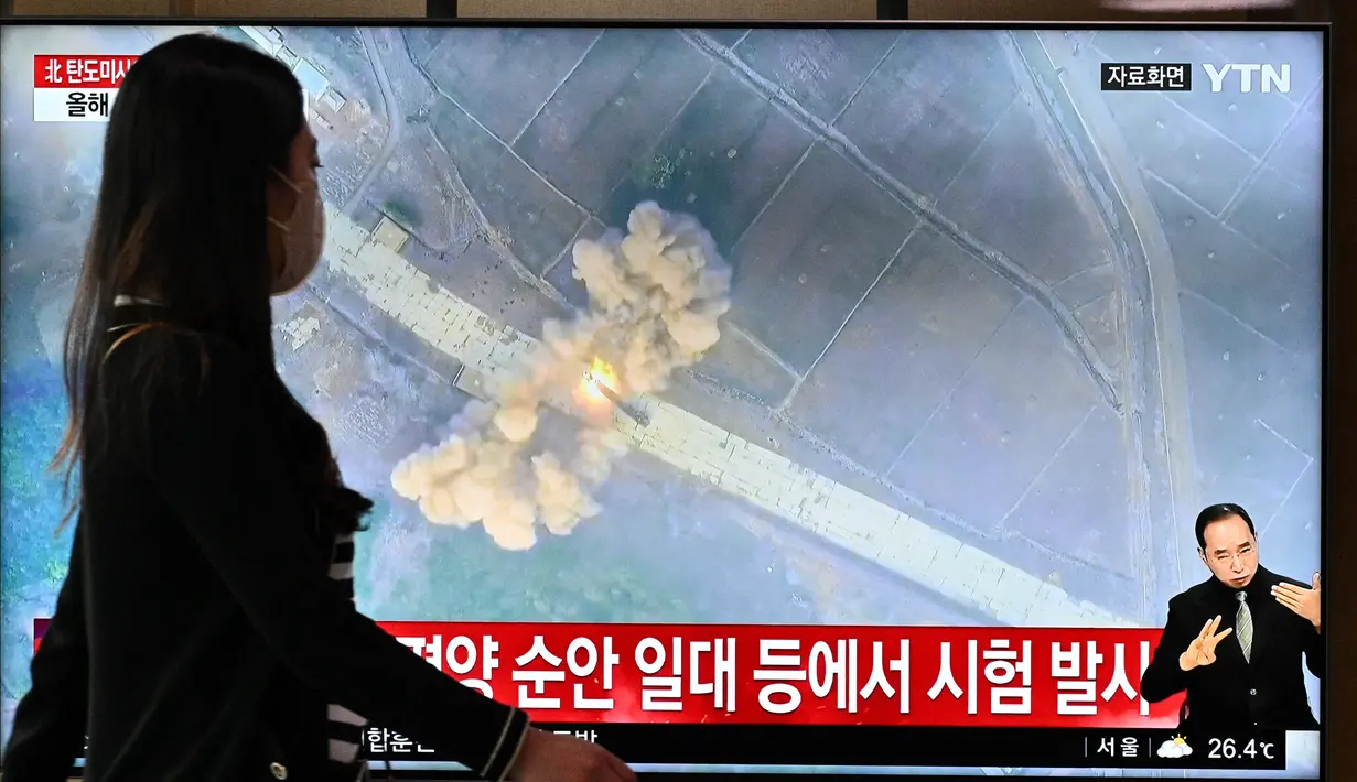 Seorang perempuan berjalan melewati layar yang menunjukkan siaran berita dengan rekaman file uji coba rudal Korea Utara, di sebuah stasiun kereta api di Seoul, Minggu (5/6/2022). Korea Utara menembakkan beberapa rudal balistik jarak pendek ke perairan lepas pantai timurnya pada hari Minggu, kata Kepala Staf Gabungan Korea Selatan. (Anthony WALLACE / AFP)