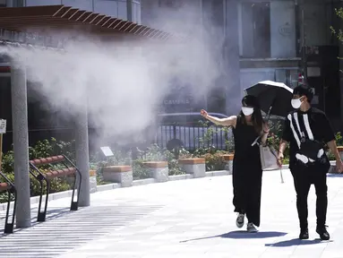 Seorang pria dan wanita mengenakan masker untuk mencegah penyebaran Covid-19 di bawah titik kabut dingin di Tokyo (12/8/2020). Menurut Badan Meteorologi Jepang, cuaca panas telah ditetapkan dengan suhu naik lebih dari 34 derajat Celcius (93,2 derajat Fahrenheit) di Tokyo. (AP Photo/Eugene Hoshiko)