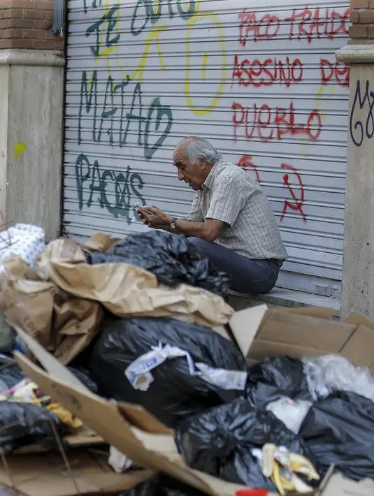 Seorang pria duduk di dekat tumpukan sampah di Santiago (14/11/2019). Protes kekerasan meletus di ibukota Chile, Santiago, pada Selasa ketika mata uang negara itu turun ke level terendah dalam sejarah. (AFP/Javier Torres)