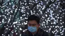 eorang pria mengenakan masker berjalan melewati pameran lampu di kawasan pusat bisnis di Beijing, Selasa (12/1/2021).  Para ahli dari WHO akan tiba di China minggu ini untuk penyelidikan yang telah lama diantisipasi mengenai asal-usul pandemi virus corona. (AP Photo/Mark Schiefelbein)