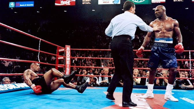 Evander Holyfield berhasil memukul jatuh Mike Tyson pada ronde keenam dalam duel perebutan sabuk juara dunia kelas berat versi WBA di MGM Grand Garden Arena, Las Vegas, 9 November 1996. Holyfield akhirnya menang TKO atas Tyson. (AFP/JEFF HAYNES)