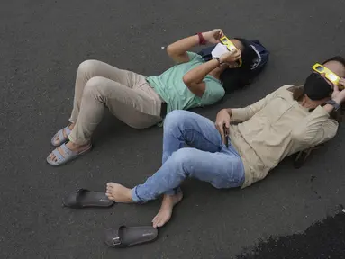 Orang-orang berbaring di tanah saat mereka menggunakan kacamata khusus untuk menyaksikan gerhana matahari hibrida di Jakarta, Kamis (20/4/2023). (AP Photo/Tatan Syuflana)