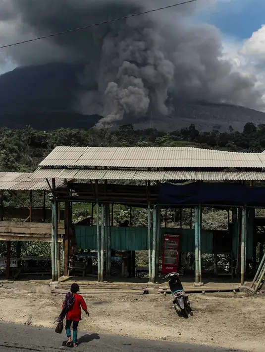 Seorang warga beraktivitas saat gunung berapi Gunung Sinabung yang memuntahkan abu tebal di Karo, Sumatra Utara (18/12). Setelah periode tidak aktif, Gunung Sinabung meletus pada tahun 2013, dan tetap sangat aktif sampai sekarang. (AFP Photo/Ivan Damanik)