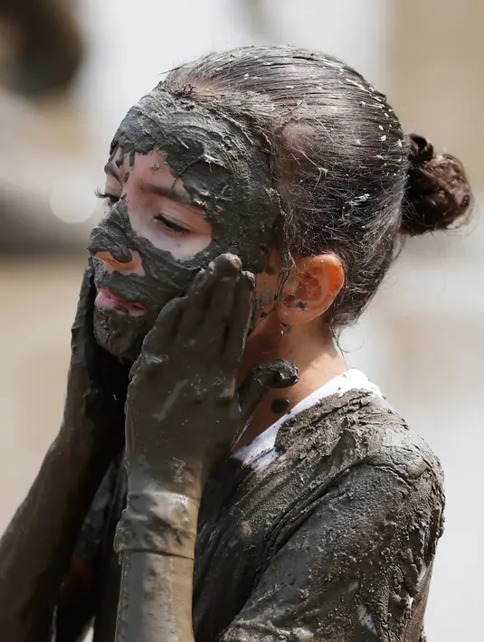 Tmiamelia Harris, 11, mengaplikasikan lumpur ke wajahnya saat Mud Day atau Hari Lumpur di Michigan, negara bagian AS, Selasa (9/7/2019). Para peserta perayaan yang menjadi tradisi setiap tahun ini merupakan anak-anak untuk agar mereka bersenang-senang selama liburan musim panas.  (AP/Carlos Osorio)