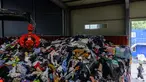 Dalam foto yang diambil pada tanggal 7 Agustus 2024 memperlihatkan seorang karyawan berjalan melewati gudang yang berisi tumpukan besar garmen, tempat tidur, mainan lunak, dan aksesori yang dikategorikan dengan cakar mekanis, sebelum diekspor ke luar negeri, di pabrik pakaian bekas di Paju, sekitar 28 km sebelah utara Seoul, Korea Selatan. (ANTHONY WALLACE/AFP)