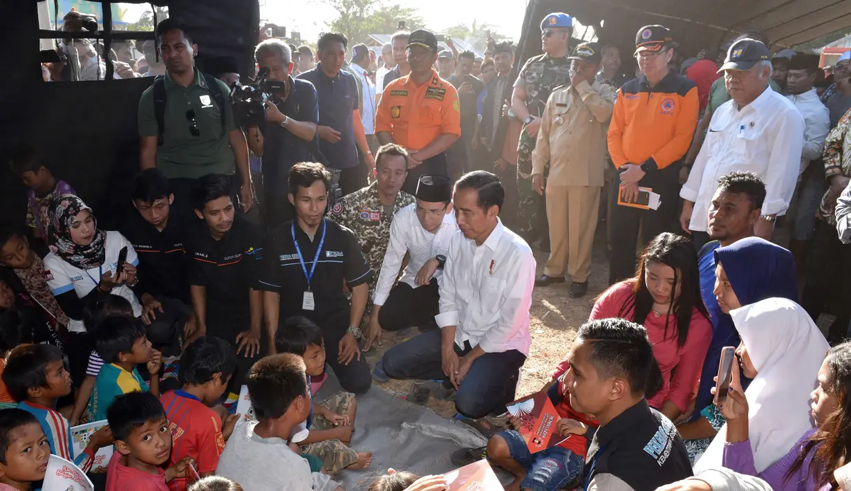 Presiden Joko Widodo atau Jokowi bersama Gubernur NTB Tuan Guru Bajang (TGB) Zainul Majdi berbincang anak-anak saat mengunjungi korban gempa di Desa Madayin, Sambelia, Lombok Timur, NTB, Senin (30/7). (Agus Suparto/Indonesian Presidential Palace/AFP)