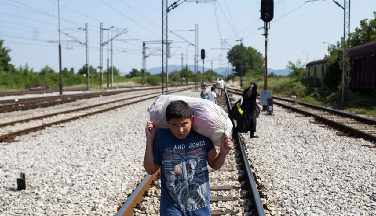 Seorang anak berjalan dengan membawa barang menyusuri rel kereta api saat perjalanan menuju Gevgelija, wilayah perbatasan Macedonia-Yunani, Kamis (9/7/2015). Mereka mencari perlindungan dengan menempuh ribuan kilometer. (AFP PHOTO/Robert ATANASOVSKI)
