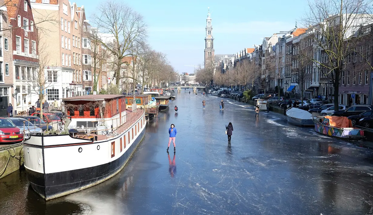 Sejumlah orang berseluncur melintasi permukaan kanal Prinsengracht yang membeku di Amsterdam, Belanda, Jumat (2/3). Cuaca dingin yang melanda Eropa selama beberapa hari terakhir membekukan kanal bersejarah tersebut. (AP/Mike Corder)