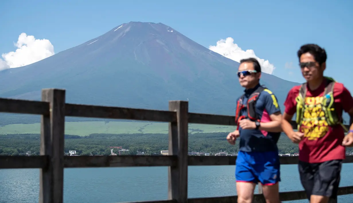 Dua pria jogging di Gunung Fuji, barat Tokyo, dengan latar belakang desa Yamanakako di prefektur Yamanashi pada 19 Juli 2021. Mendaki Gunung Fuji bukan hal yang mudah, tetapi pemandangan matahari terbit di atas lautan awan adalah hadiah terindah bagi yang mencapai puncak. (Charly TRIBALLEAU/AFP)
