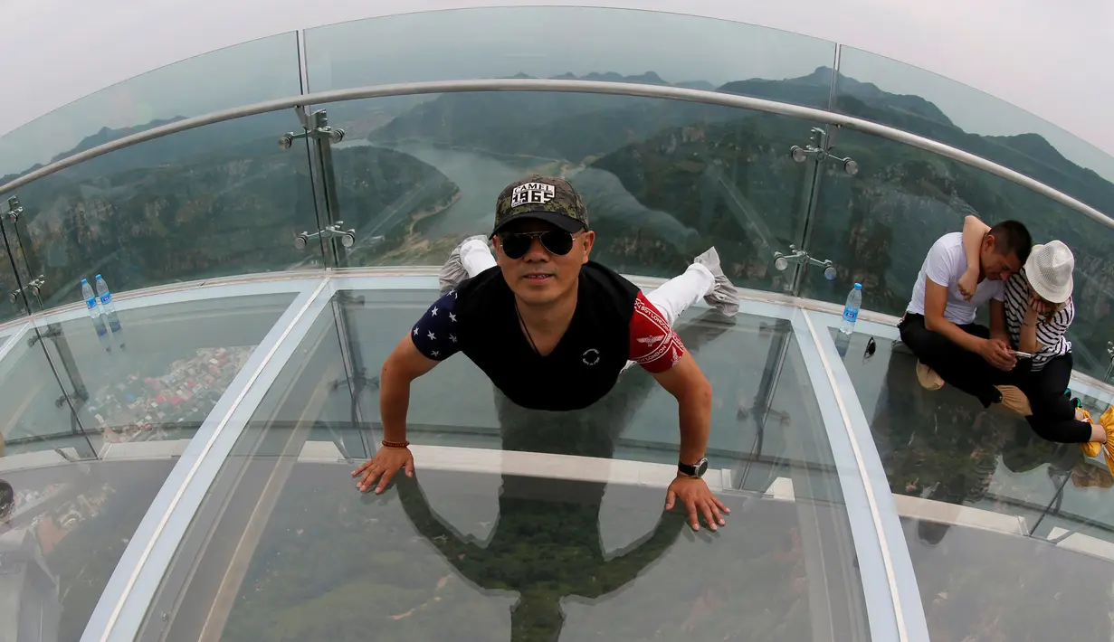 Seorang pria berpose saat mengunjungi platform kaca di Shilin Gorge, Beijing, Cina, (27/5). Objek wisata baru di China ini berada di ketinggian 768 meter dan berjarak 400 meter dari dasar jurang. (REUTERS/Kim Kyung-Hoon)