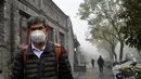 Seorang pria yang mengenakan masker berjalan di sepanjang jalan yang berkabut dan tercemar di Beijing, Sabtu (6/11/2021). Jalan raya dan taman bermain sekolah di Beijing ditutup pada Jumat (5/11) karena polusi kabut asap yang tebal, setelah China meningkatkan produksi batu bara. (JADE GAO/AFP)