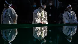Penganut shinto dari Kuil Teppozu Inari berdiri di samping kolam sebelum mandi sebelum mandi dengan air dingin untuk mensucikan jiwa selama ritual Tahun Baru di Tokyo, Jepang, Minggu (9/1/2022). Mereka bersama-sama bertepuk tangan dan bernyanyi sebelum masuk ke pemandian air es. (Philip FONG/AFP)