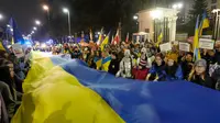 Para peserta membawa bendera raksasa Ukraina untuk memperingati satu tahun invasi Rusia ke Ukraina di depan Kedutaan Besar Rusia, Warsawa, Polandia, 24 Februari 2023. (AP Photo/Czarek Sokolowski)