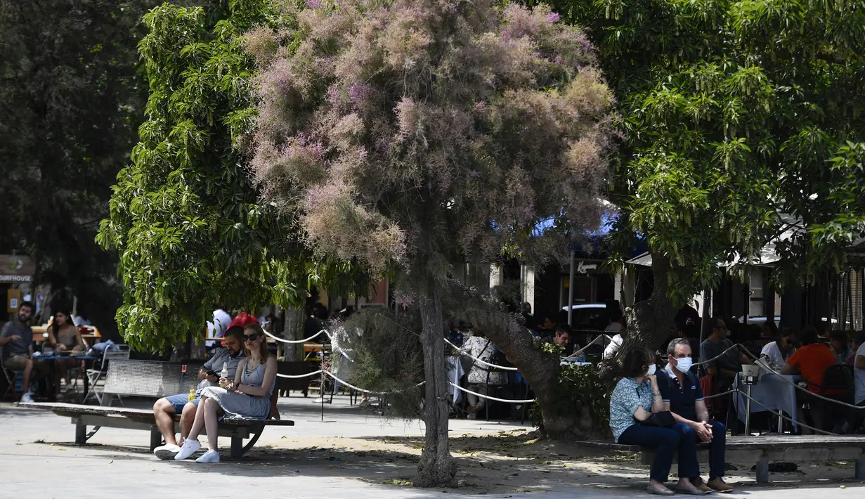Orang-orang duduk di kawasan pejalan kaki di Pantai Barceloneta, Barcelona, Minggu (6/6/2021). Spanyol akan mengizinkan semua pelancong yang divaksinasi untuk mengunjungi negara itu mulai 7 Juni, dengan tujuan kembali menghidupkan industri perjalanan yang terpukul pandemi Covid-19. (Pau BARRENA/AFP)