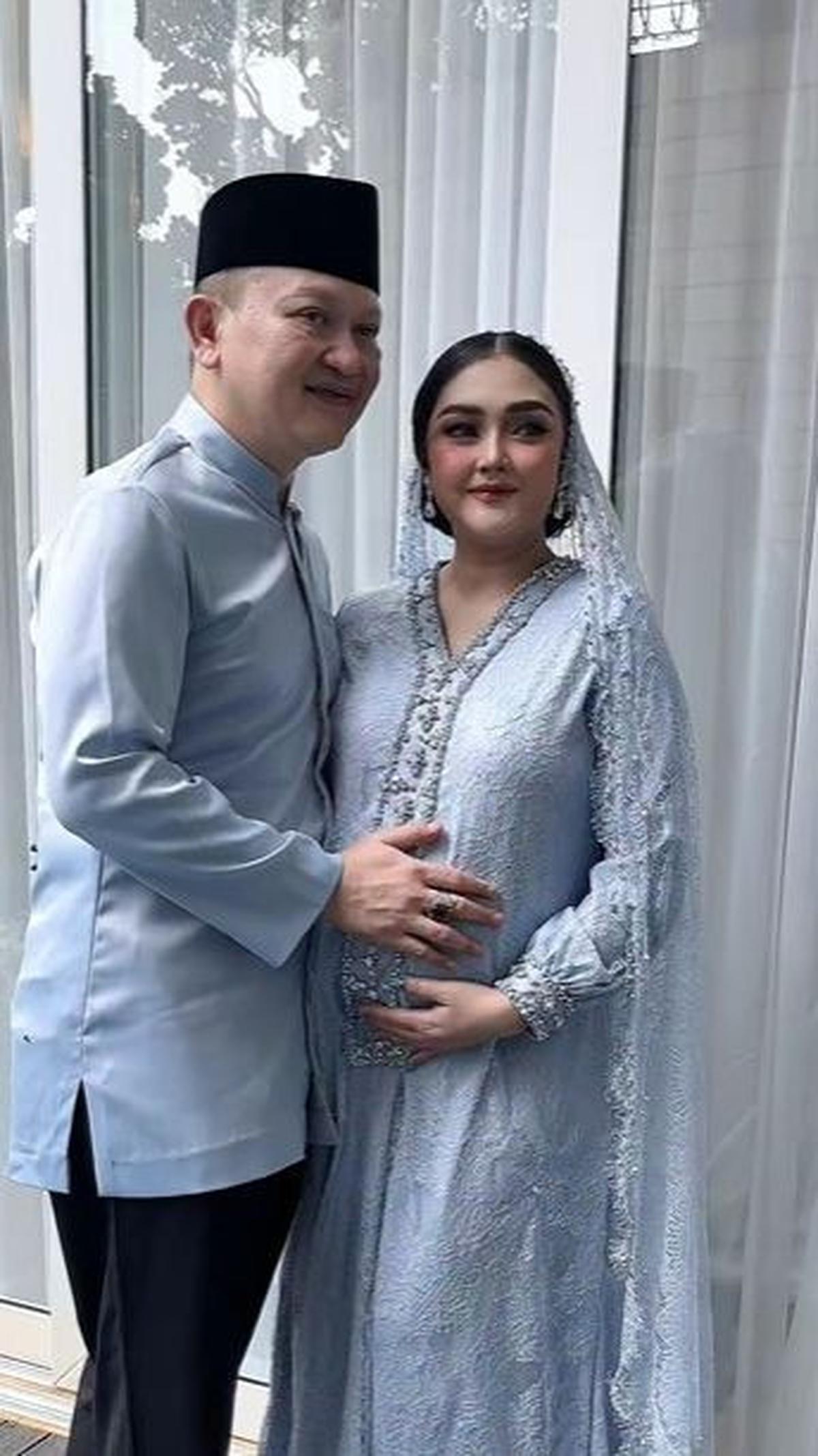 Pada momen itu Suci terlihat cantik mengenakan busana berwarna biru. Sang suami pun nampak gagah dengan baju warna senada ditambah peci hitam.