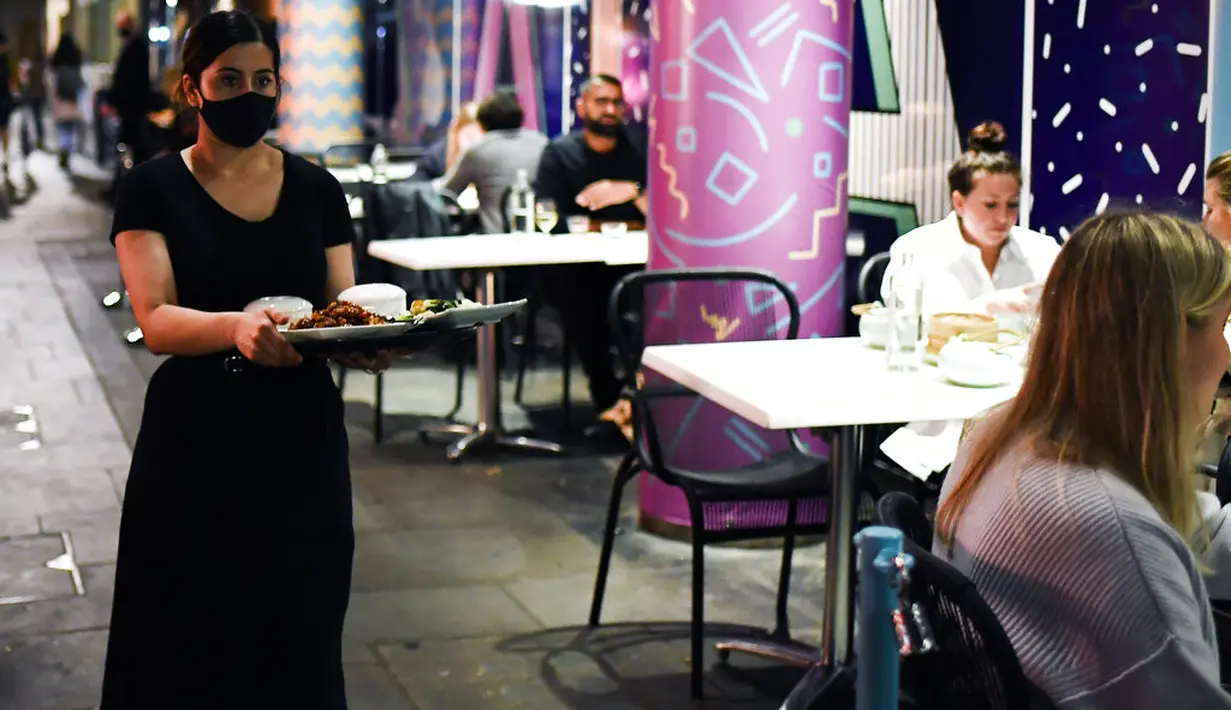 Pramusaji mengenakan masker saat melayani pelanggan di luar restoran di Soho, London, Selasa (22/9/2020). Perdana Menteri Inggris, Boris Johnson, telah mengumumkan bahwa pub dan restoran tutup pada pukul 10 malam, karena lonjakan kasus virus corona di seluruh Inggris. (AP Photo / Alberto Pezzali)