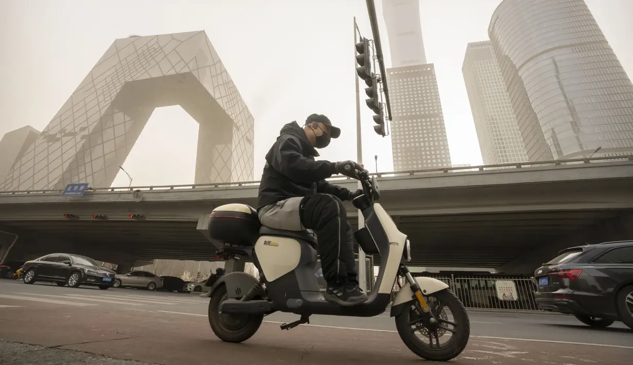 <p>Seorang pria yang mengenakan masker mengendarai skuter di sepanjang jalan di kawasan pusat bisnis di Beijing, Rabu, 22 Maret 2023. (AP Photo/Mark Schiefelbein)</p>