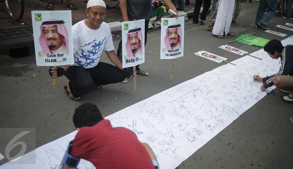 Seorang pria memegang poster sambil mengamati pengunjung Car Free Day (CFD) menandatangani spanduk berisi petisi mendukung kedatangan Raja Arab Saudi, Salman bin Abdulazis Al Saud, di Bundaran HI, Jakarta, Minggu (26/2). (Liputan6.com/Faizal Fanani)