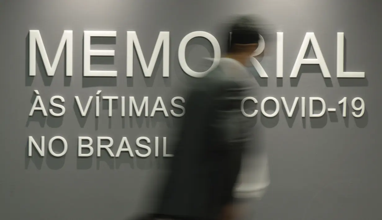 Seorang pria melewati dinding yang bertuliskan dalam bahasa Portugis "Memorial untuk para korban COVID-19 di Brasil," di gedung Senat Brasil di Brasilia, 15 Februari 2022. Monumen tersebut terdiri dari 27 prisma, mewakili negara bagian Brasil. (AP/Claudio Reis)