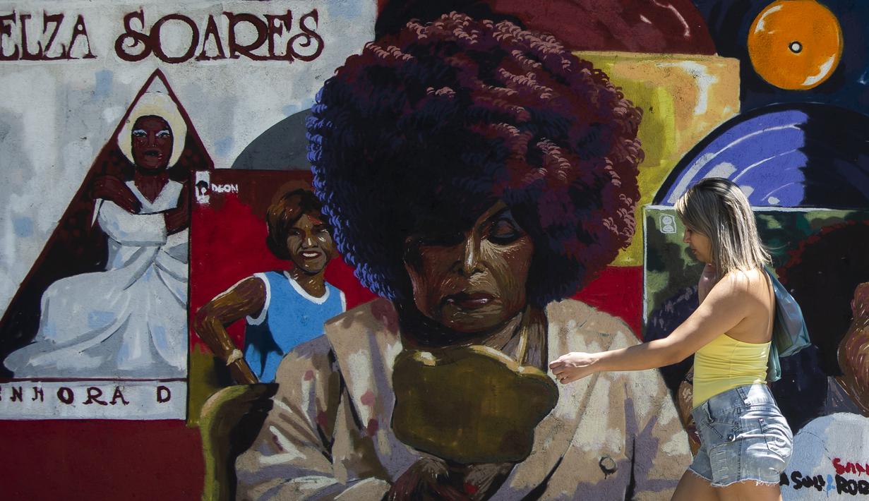 Seorang wanita melewati lukisan perkotaan yang menampilkan gambar penyanyi-penulis lagu Elza-Soares, yang dibuat oleh seniman Cafe dan produser Pedro Rojao, di Rio de Janeiro, 17 November 2021. Brasil menyambut Hari Kesadaran Kulit Hitam yang diperingati setiap 20 November. (AP Photo/Bruna Prado)