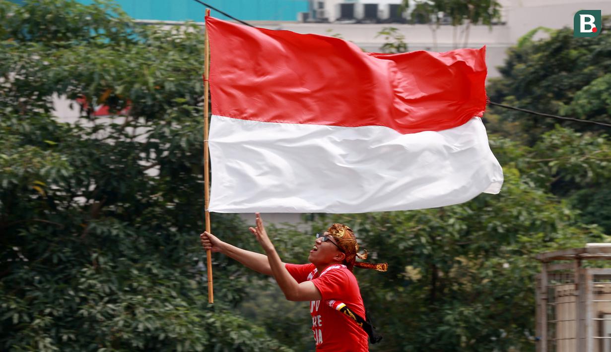 Seorang masyarakat membawa bendera Merah Putih saat menyambut Timnas Indonesia U-22 dan kontingen Indonesia untuk SEA Games 2023 saat pawai Kira87uara yang berlangsung dari Kemenpora hingga GBK, Jakarta, Jumat (19/05/2023). (Bola.com/M Iqbal Ichsan)