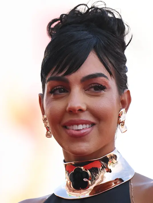 <p>Georgina Rodriguez tersenyum sambil berpose untuk fotografer setibanya di pemutaran perdana film 'Tar' selama Venice Film Festival ke-79 di Venesia, Italia (1/9/2022). Georgina merias rambut cokelatnya menjadi sanggul. (AFP/Tiziana Fabi)</p>