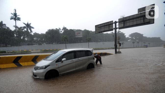 Seorang pria mendorong mobil yang mogok saat banjir menggenangi Jalan Tol JORR di kawasan TB Simatupang, Jakarta Selatan, Sabtu (20/2/2021). Banjir terjadi akibat luapan Kali Serua yang berada di pinggir jalan tol. (merdeka.com/Arie Basuki)