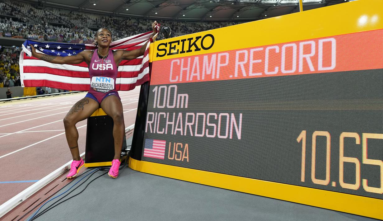 Pelari Amerika Serikat, Sha’Carri Richardson berfoto di samping papan catatan waktu setelah berhasil menorehkan rekor baru pada final 100 meter putri Kejuaraan Dunia Atletik 2023 di National Athletics Centre, Budapest, Hungaria, pada 22 Augustus 2023. (AP Photo/Bernat Armangue)