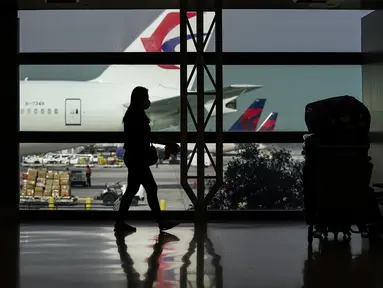 Siluet pelancong dengan masker di samping kopernya di Bandara Internasional Los Angeles di Los Angeles, California, 23 November 2020. Sekitar 1 juta orang Amerika memadati bandara dan pesawat menjelang libur Thanksgiving pekan ini bahkan saat kematian akibat COVID-19 melonjak. (AP Photo/Jae C. Hong)