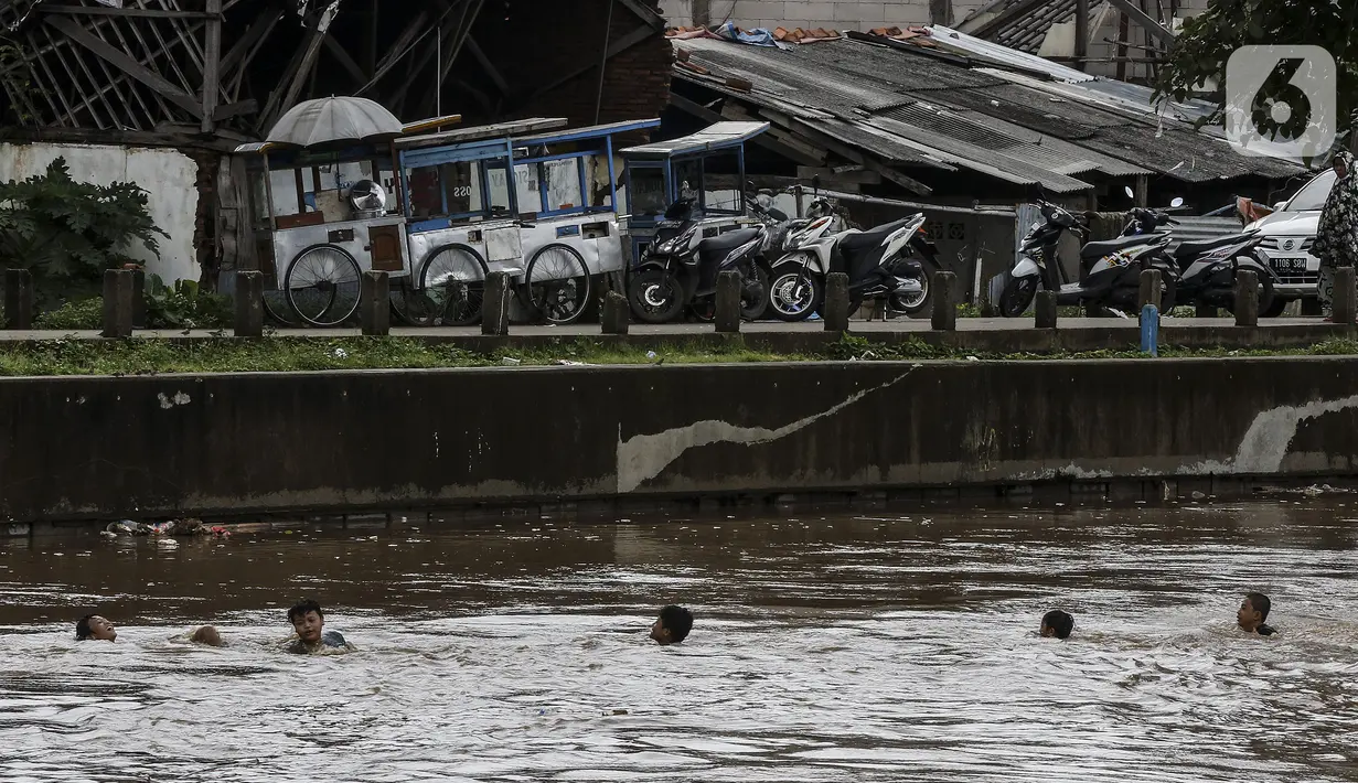 Anak-anak berenang di Sungai Ciliwung saat banjir melanda Jalan Bina Warga Rt 005/Rw 07 Kelurahan Rawa Jati, Jakarta, Senin (8/2/2021). Banjir setinggi 60-190 cm tersebut disebabkan oleh luapan air Sungai Ciliwung dan curah hujan Jakarta yang tinggi. (Liputan6.com/Johan Tallo)