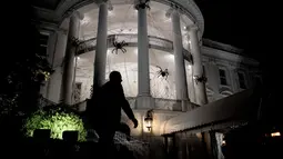 Petugas keamanan berjalan di depan pelataran Gedung Putih yang dipenuhi laba-laba raksasa di Washington DC, AS, Sabtu (28/10). Laba-laba raksasa tersebut merupakan boneka yang sengaja dipasang dalam rangka menyambut Halloween. (Brendan Smialowski / AFP)