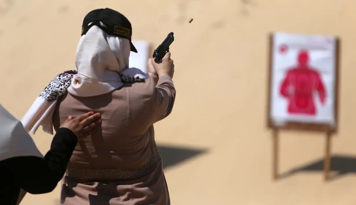 Seorang wanita Palestina memegang pistol saat melepas tembakan ke target sasaran selama mengikuti pelatihan dengan anggota perlindungan dan keamanan Hamas di Khan Younis di Jalur Gaza, Minggu (24/7). (REUTERS/ Ibraheem Abu Mustafa)