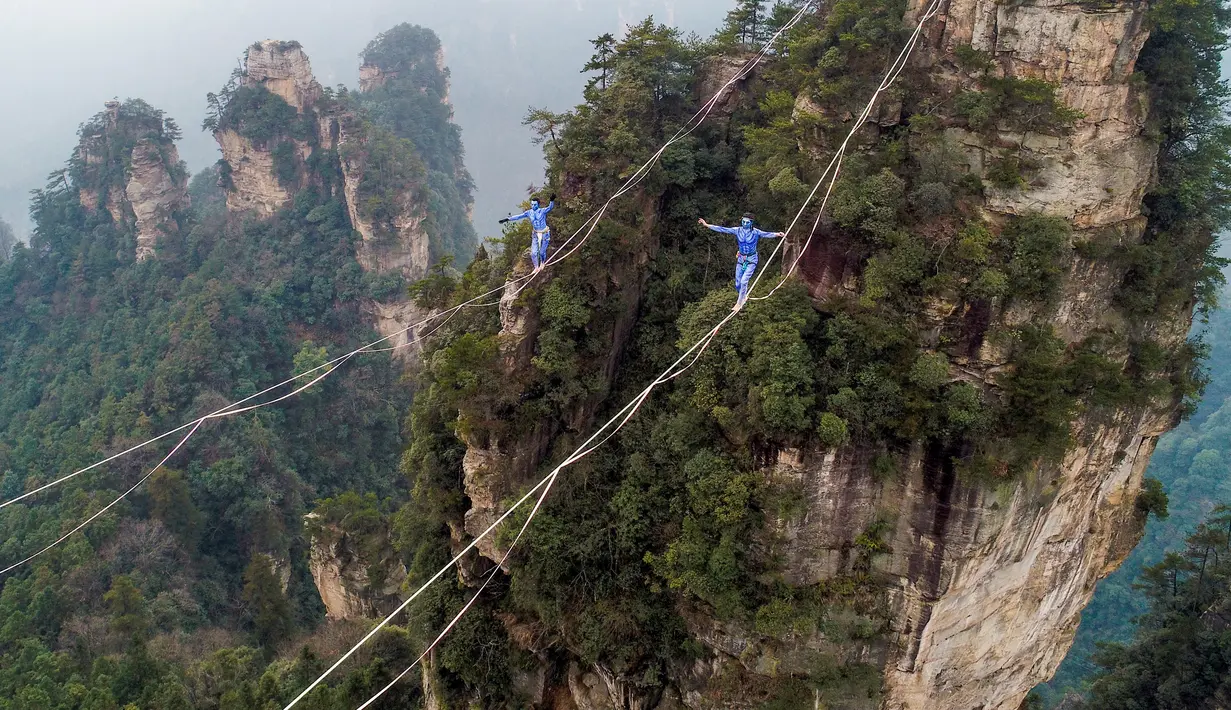 Dua kontestan berpakaian karakter Avatar berpacu sepanjang slackline di Pegunungan Huangshizhai di Zhangjiajie, Hunan, China, Minggu (23/12). Aksi tersebut dilakukan di Situs Warisan Dunia Wulingyuan atau Pegunungan Melayang. (STR/AFP)