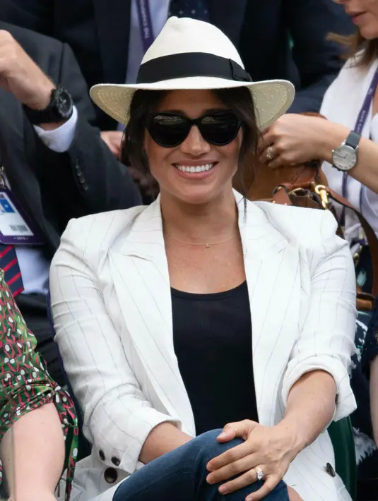 Meghan Markle menyaksikan sahabatnya yang juga petenis AS Serena Williams melawan Kaja Juvan dari Slovakia pada babak kedua Wimbledon di All England Lawn Tennis Club, London, Kamis (4/7/2019). Meghan Markle menyempurnakan penampilannya dengan topi berwarna senada dan kacamata hitam. (AP/Tim Ireland)