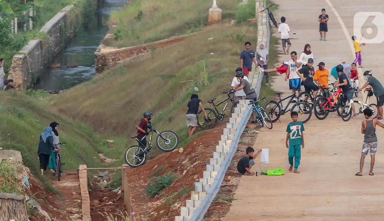 Warga menyeberangi selokan untuk bersepeda di kawasan Tol Serpong Kunciran, Ciputat, Tangerang Selatan, Kamis (25/6/2020). Pembangunan tol yang belum rampung dimanfaatkan sejumlah warga beraktivitas selama pandemi Covid-19. (Liputan6.com/Fery Pradolo)