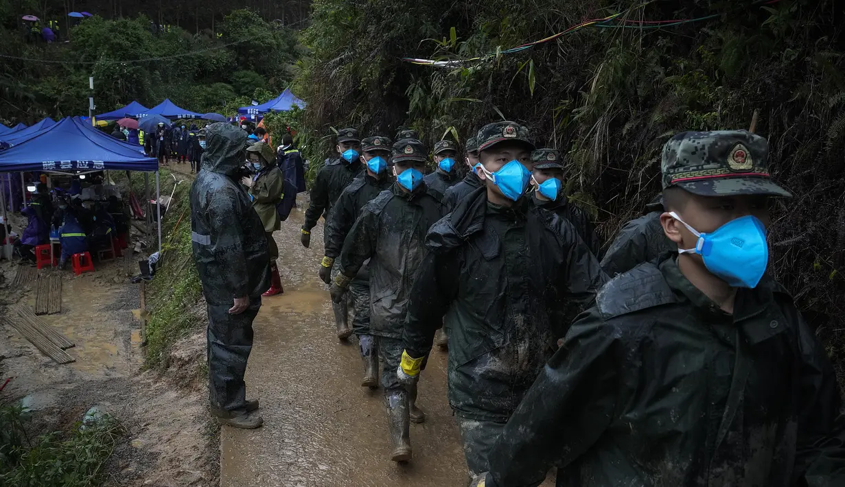 Tentara mengenakan masker wajah berbaris di jalan lereng bukit yang basah kuyup dekat lokasi kecelakaan pesawat Boeing 737-800 milik China Eastern Airlines untuk mencari kotak hitam kedua di desa Molang, di provinsi Guangxi, China barat daya, Rabu (24/3/2022). (AP Photo/Ng Han Guan)