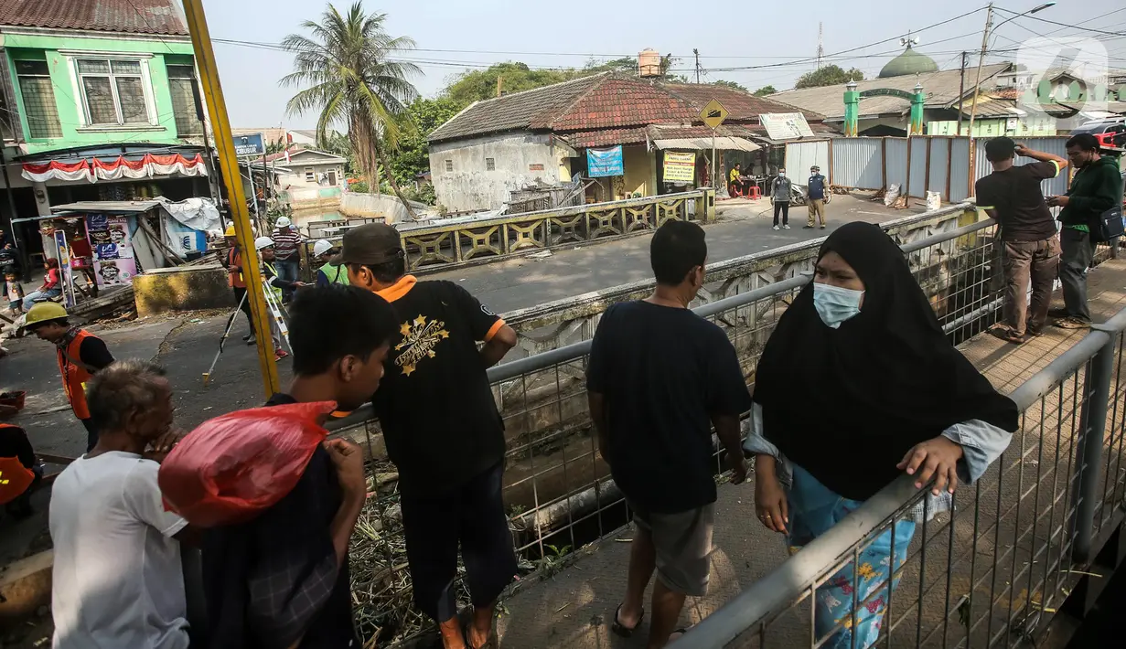 Warga beraktivitas melewati area sekitar proyek revitalisasi Jembatan Cibubur, Jakarta, Selasa (2/8/2022). Revitalisasi dilakukan untuk mengantisipasi risiko banjir akibat rendahnya muka jembatan serta risiko kecelakaan akibat tidak adanya trotoar. (Liputan6.com/Faizal Fanani)