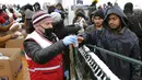 Para imigran menerima bantuan makanan saat hujan salju di Kamp Lipa, luar Bihac, Bosnia, Jumat (8/1/2021). Cuaca bersalju dan musim dingin telah membawa lebih banyak penderitaan bagi ratusan imigran yang terjebak selama berhari-hari di kamp tersebut. (AP Photo/Kemal Softic)
