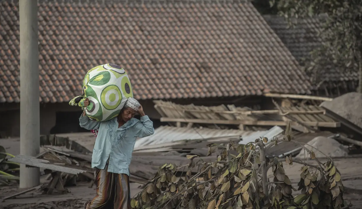 Seorang warga menyelamatkan barang-barangnya di area yang tertutup abu vulkanik setelah letusan gunung Semeru di desa Sumber Wuluh di Lumajang, Jawa Timur, Minggu (5/12/2021). (AFP /Juni Kriswanto)