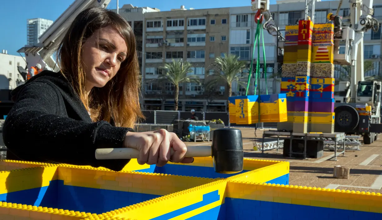 Seorang wanita menyusun LEGO yang akan dibuat menjadi menara di Lapangan Rabin di Tel Aviv, Israel, Rabu (27/12). Menara ini dibangun untuk menghormati penggemar LEGO berusia 8 tahun, Omer Sayag yang meninggal pada tahun 2014 silam. (AFP Photo/Jack Guez)