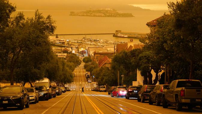 Seorang pria melintasi Hyde Street dengan Pulau Alcatraz dan Fisherman's Wharf terlihat pada latar belakang di San Francisco, Amerika Serikat, Rabu (9/9/2020). Kebakaran hutan di seluruh Barat mengakibatkan langit San Francisco hingga Seattle berwarna oranye yang menakutkan. (AP Photo/Eric Risberg)
