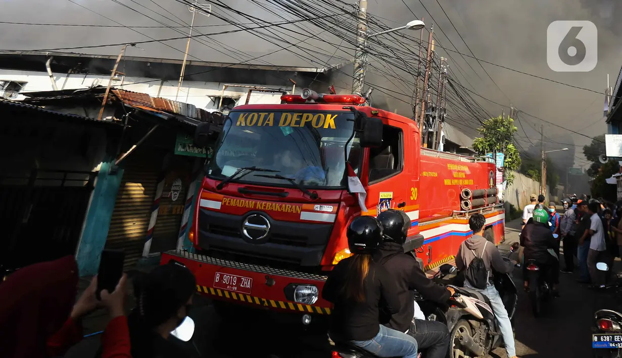 Pengendara melintas saat petugas berusaha memadamkan api  di Gudang JNE Express yang terbakar di Jalan Pekapuran Raya, Depok, pada Senin (12/9/2022). Polisi juga berada di sekitar lokasi untuk mengatur lalu lintas. (Liputan6.com/Herman Zakharia)