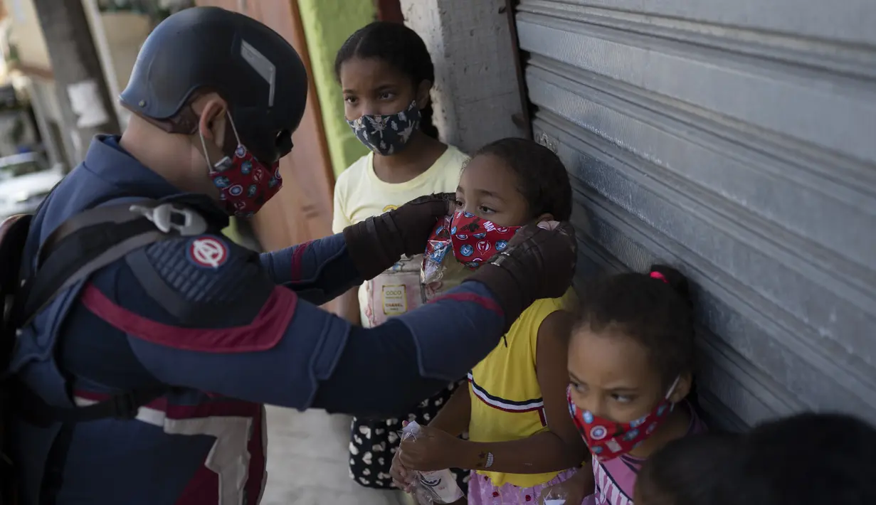 Petugas polisi militer Everaldo Pinto, berkostum superhero Captain America, memakaikan masker pada anak-anak di tengah pandemi COVID-19 di Petropolis, Rio de Janeiro, Brasil, Kamis (15/4/2021). Pinto memberitahu anak-anak tentang perlunya melindungi diri dari virus corona. (AP Photo/Silvia Izquierdo