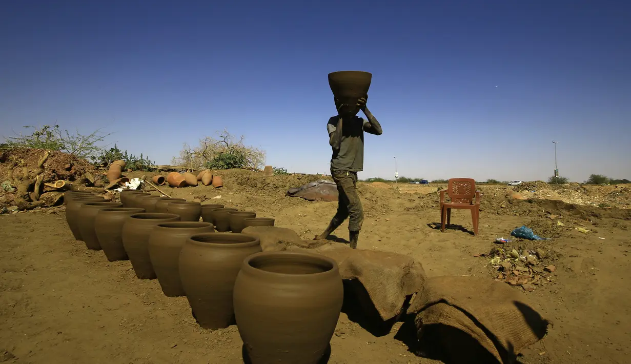 Seorang pekerja Sudan membawa pot tanah liat di bengkel tembikar di Omdourman, di pinggiran barat ibu kota Khartoum (19/1/2022). Pot tanah liat tersebut nantinya akan dipajang untuk dijual. (AFP/Ashraf Shazly)