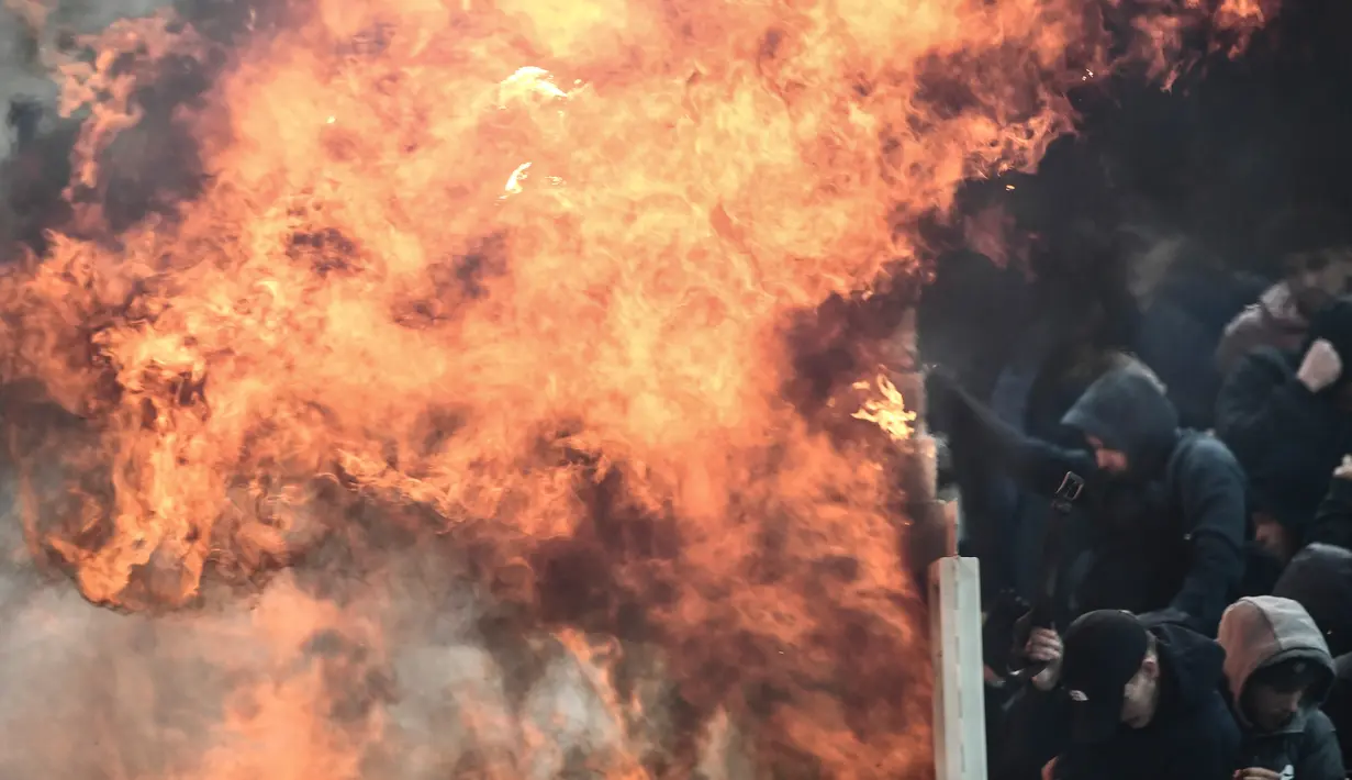 Suporter Ajax Amsterdam mencoba untuk melindungi diri dari ledakan bom molotov selama bentrokan dengan polisi anti huru-hara Yunani sebelum pertandingan Liga Champions melawan AEK Athena di Stadion Olimpiade Athena, Selasa (27/11). (Aris Messinis/AFP)