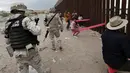 Tentara mengawasi warga dan anak-anak yang bermain jungkat-jungkit di antara pagar pemisah Meksiko dengan Amerika Serikat, Ciudad de Juarez, Meksiko, Minggu (28/7/2019). Jungkat-jungkit tersebut dirancang seorang profesor arsitektur California, Ronald Rael. (AP Photo/Christian Chavez)